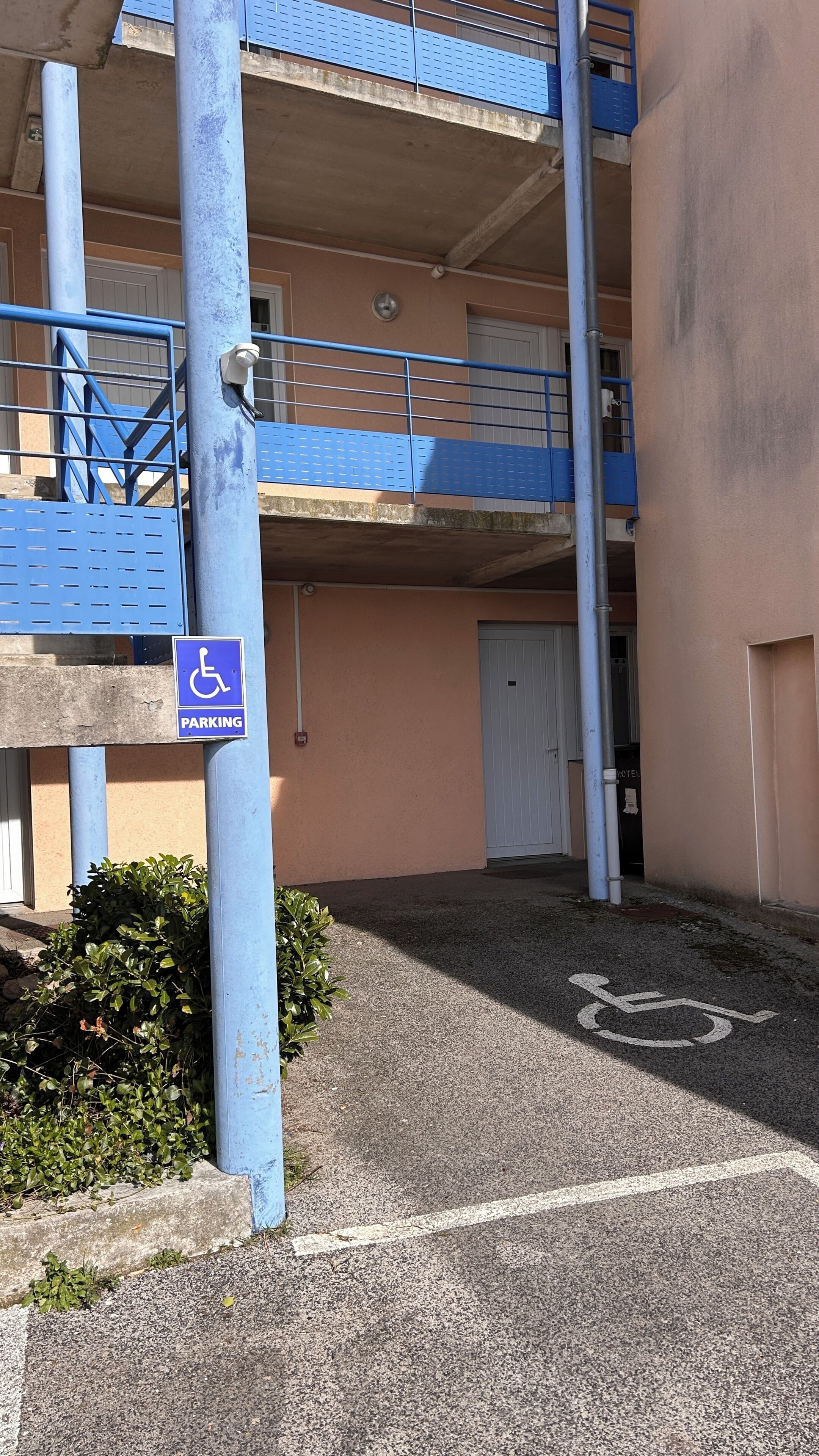 A multi-level parking area with a disabled parking sign, a wheelchair symbol on the ground, and a building with a beige facade.