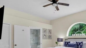 Quarto com cama king-size, ventilador de teto, janela com vista para o verde, closet espaçoso e banheiro com porta de vidro.