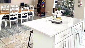 Uma cozinha moderna com ilha central, armários brancos e uma área de jantar com cadeiras brancas e mesa de madeira.