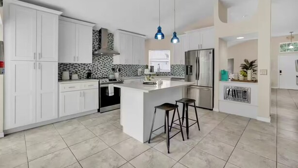 Uma cozinha moderna com armários brancos, uma ilha central com banquetas, uma geladeira de aço inoxidável e um painel de parede com padronagem.