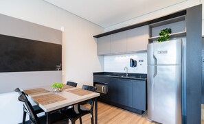 A modern kitchen with a built-in oven, a refrigerator, and a sink. There is a dining table with chairs and a small plant on it. - Estadia em prédio com piscina a poucos passos da praia em Florianópolis - STIs (Florianópolis)