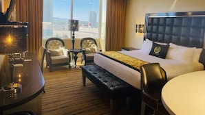 A hotel room with a large bed, a desk, two armchairs, a small table, and a view of the cityscape.