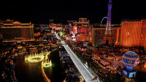 A nighttime cityscape with illuminated buildings, a river with fountains, and a prominent tower.