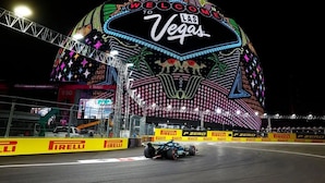 A Formula 1 car on a racetrack with a large illuminated sign reading "WELCOME TO LAS VEGAS" in the background.