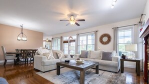 A spacious living room with a wooden coffee table, a beige sofa, and a dining area with a wooden table and chairs. - The Retreat at Paradise Hills  (Dandridge)