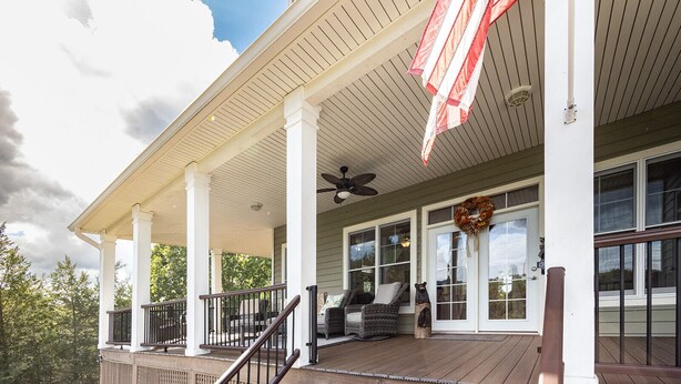 A covered porch with a ceiling fan, a wooden deck, and a view of the surrounding trees. - The Retreat at Paradise Hills  (Dandridge)