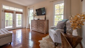 A spacious living room with hardwood floors, a large TV, a wooden dresser, a grey sofa, and a cowhide rug. - The Retreat at Paradise Hills  (Dandridge)