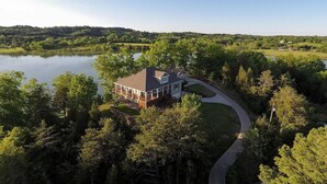 A house with a wrap-around porch, situated near a lake surrounded by dense trees. - The Retreat at Paradise Hills  (Dandridge)