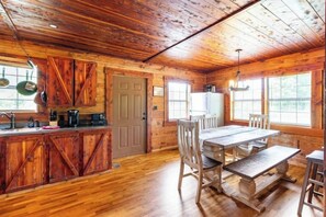 A rustic cabin interior with a wooden dining table, benches, and a kitchen area with wooden cabinets and a refrigerator. - Martin Springs Cabin. (South Pittsburg)