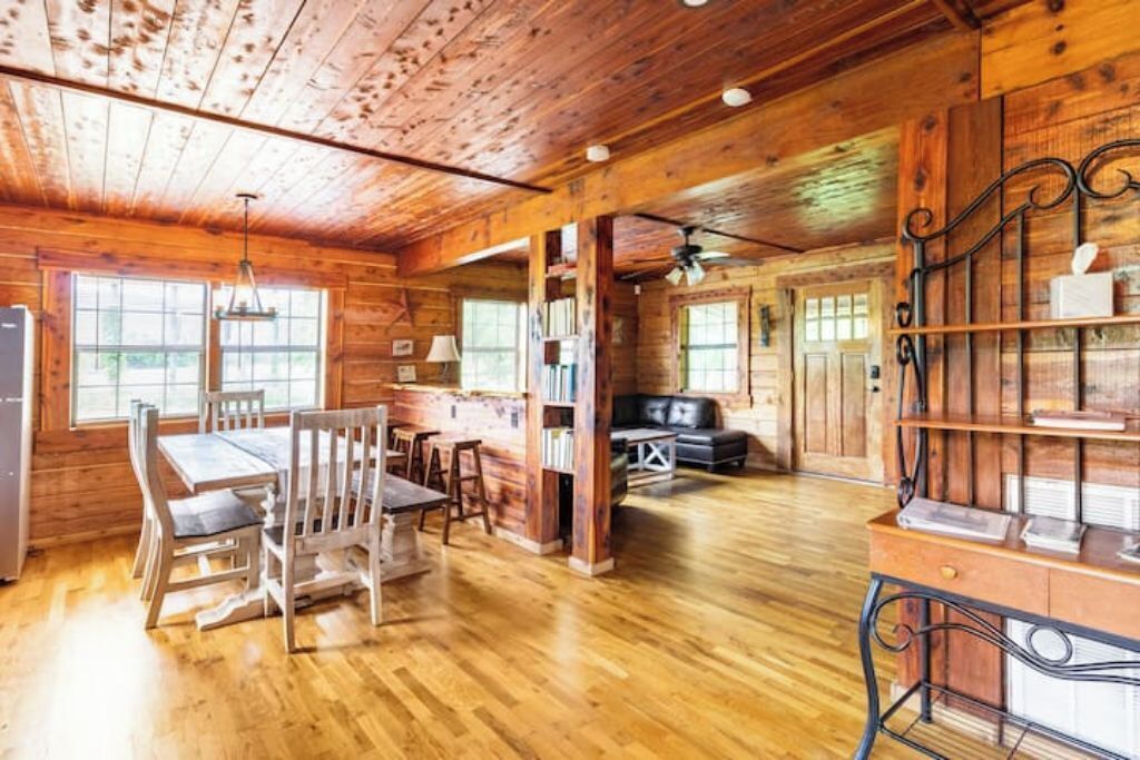 A rustic wooden cabin interior with a dining area, bookshelves, and a seating area.