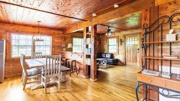 A rustic wooden cabin interior with a dining area, bookshelves, and a seating area.