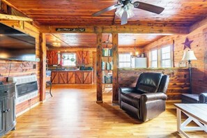 A cabin interior with a wooden ceiling, a leather recliner, a dining table, and a kitchen area with a stove and refrigerator. - Martin Springs Cabin. (South Pittsburg)