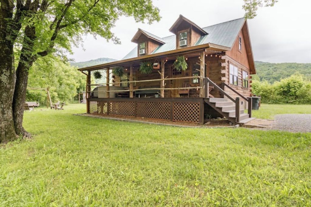 A wooden cabin with a porch, steps, and a view of the surrounding forest.