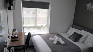 A hotel room with a bed, a desk with a telephone, a chair, and a window with a view of greenery. - Premium Serviced Accommodation Nottingham - Standard Double Room+Private Ensuite (Nottingham)
