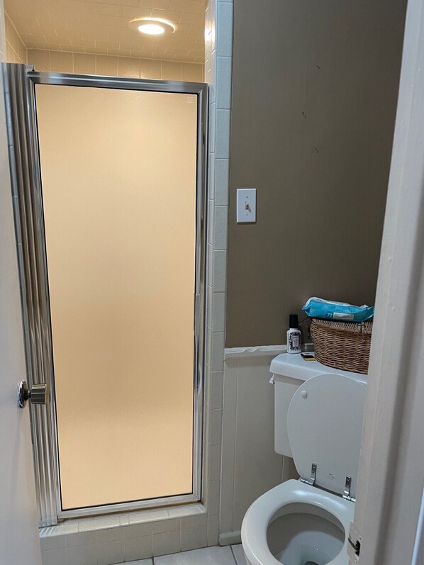A bathroom with a shower enclosure, toilet, and a basket on the wall.