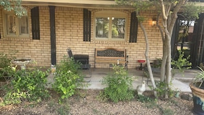 Ein Backsteinhaus mit Veranda, Bank und Garten, inklusive Pflanzen und Vogelbad.