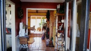 Ein Flur mit Fliesenboden, der zu einem Zimmer mit Bett und Fenster führt. Auf der rechten Seite befinden sich Regale mit verschiedenen Gegenständen.