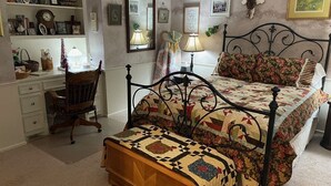Ein Schlafzimmer mit einem Bett, einem Sessel, einem Schreibtisch und Regalen mit verschiedenen Gegenständen.
