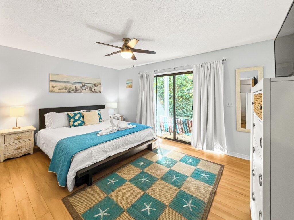 A bedroom with a bed, a ceiling fan, a window with curtains, a nightstand, and a dresser.