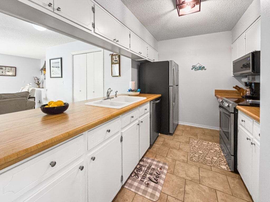 Eine kleine Küche mit weißen Schränken, einer Holz Arbeitsplatte, einem Kühlschrank, einer Mikrowelle und einem Backofen.