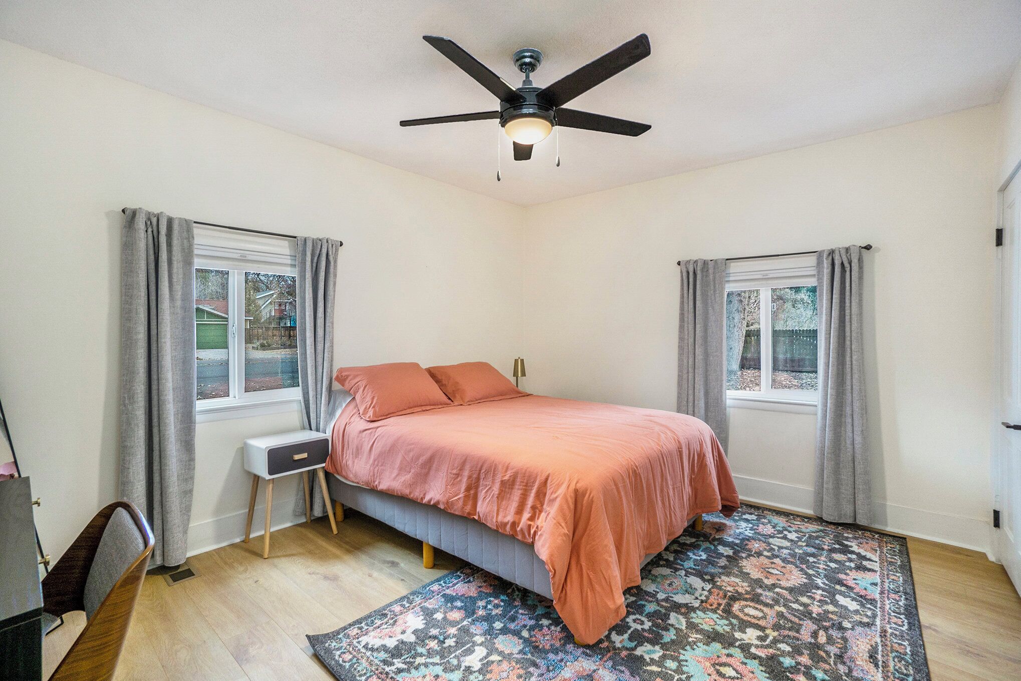A bedroom with a bed, a desk, a ceiling fan, and a window with curtains.