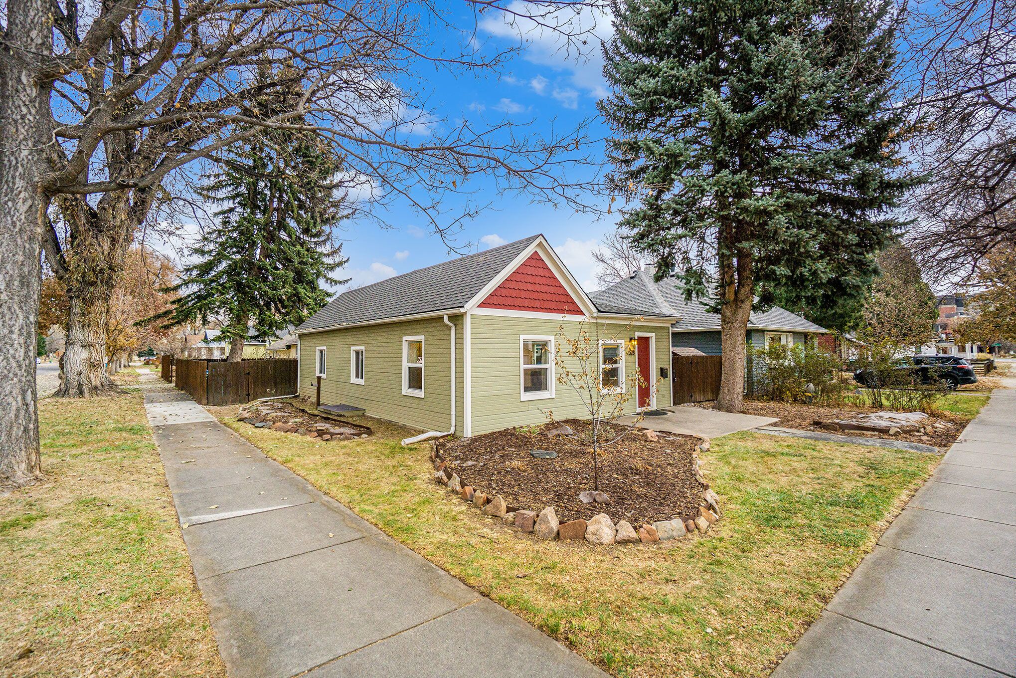 A single-story house with a red roof, a front yard with a small tree, and a sidewalk.