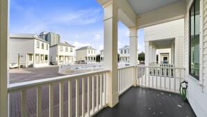 A covered balcony with white railings, a paved ground, and a view of neighboring buildings. - By The Beach: 2BR House (Orange Beach)