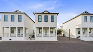 A row of three two-story houses with a uniform architectural style, featuring a central entrance with a porch and a small staircase leading to the main door. - By The Beach: 2BR House (Orange Beach)