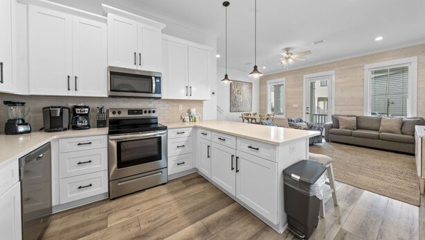A modern kitchen with white cabinets, stainless steel appliances, and a central island. - By The Beach: 2BR House (Orange Beach)