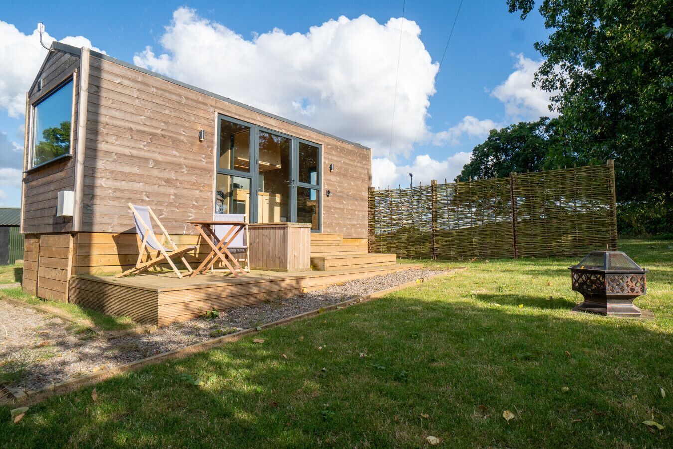 A wooden cabin with large windows, a deck, and outdoor seating.