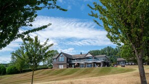 A large, modern house with a prominent balcony and a spacious lawn.