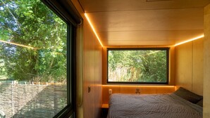 A bedroom with a large window, wooden walls, and a bed with a textured blanket.