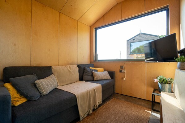 Una habitación acogedora con sofá, televisión sobre un mueble bajo y ventana con vista a un edificio.