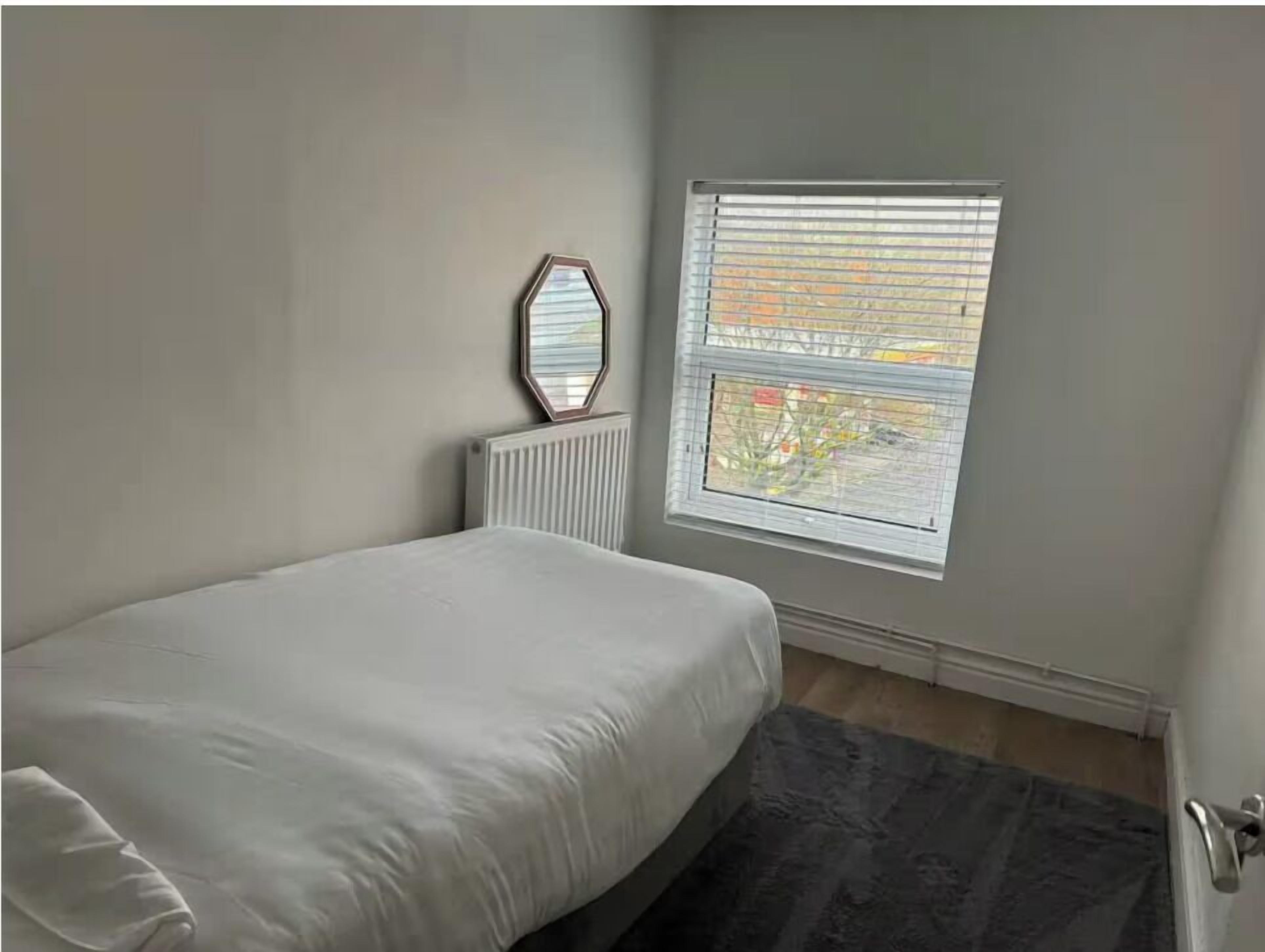 Un dormitorio con cama, un radiador, una ventana con persianas y un espejo en la pared.