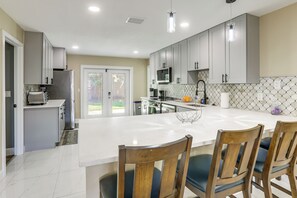 A modern kitchen with white cabinets, a central island, and a dining area with wooden chairs.