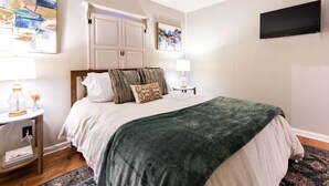 A bedroom with a bed, two bedside tables, a TV, and artwork on the walls.