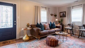 A living room with a brown leather sofa, patterned rug, ottoman, and a small side table with a globe.