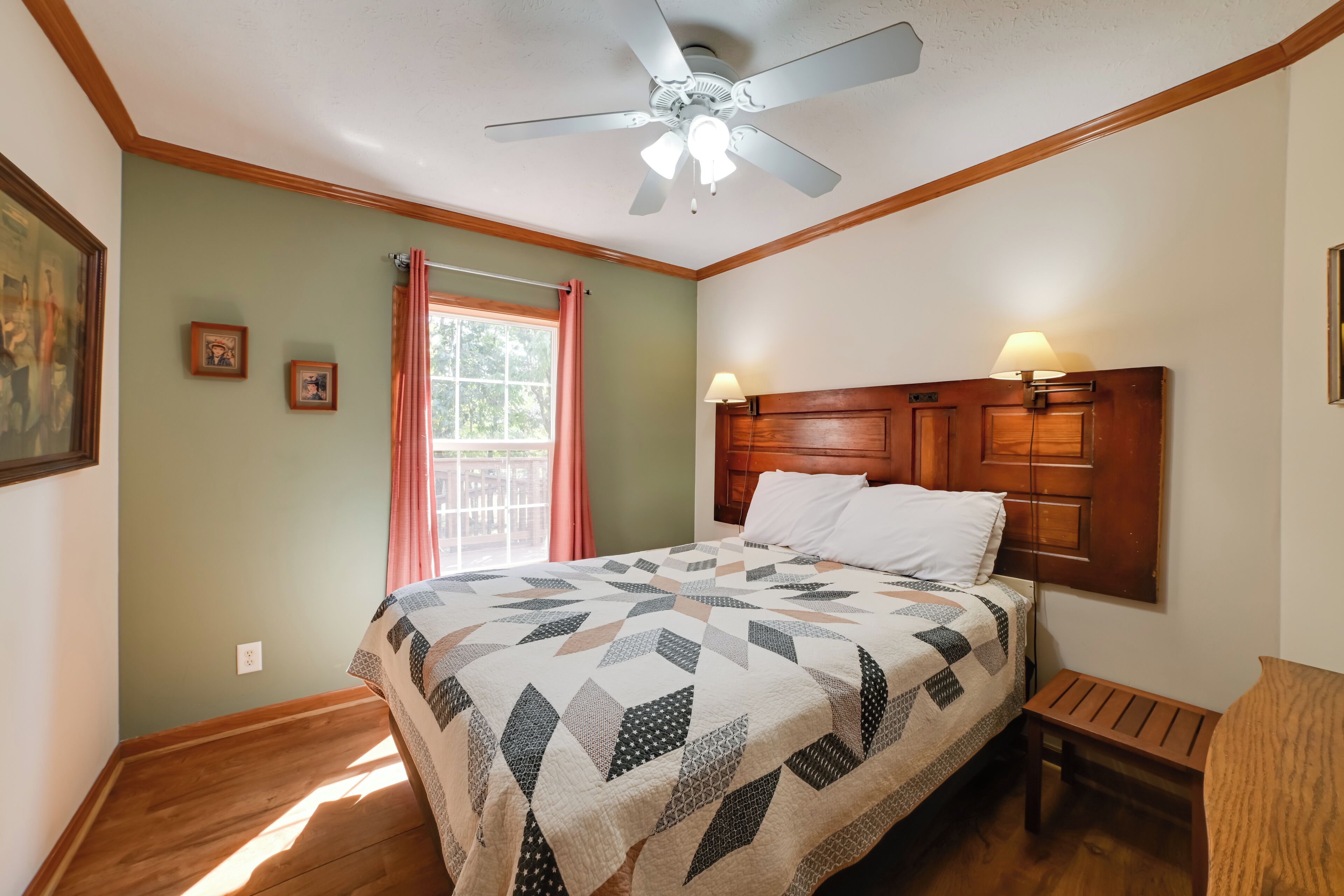 Une chambre à coucher avec un lit, une tête de lit en bois, un ventilateur de plafond et une fenêtre avec des rideaux.