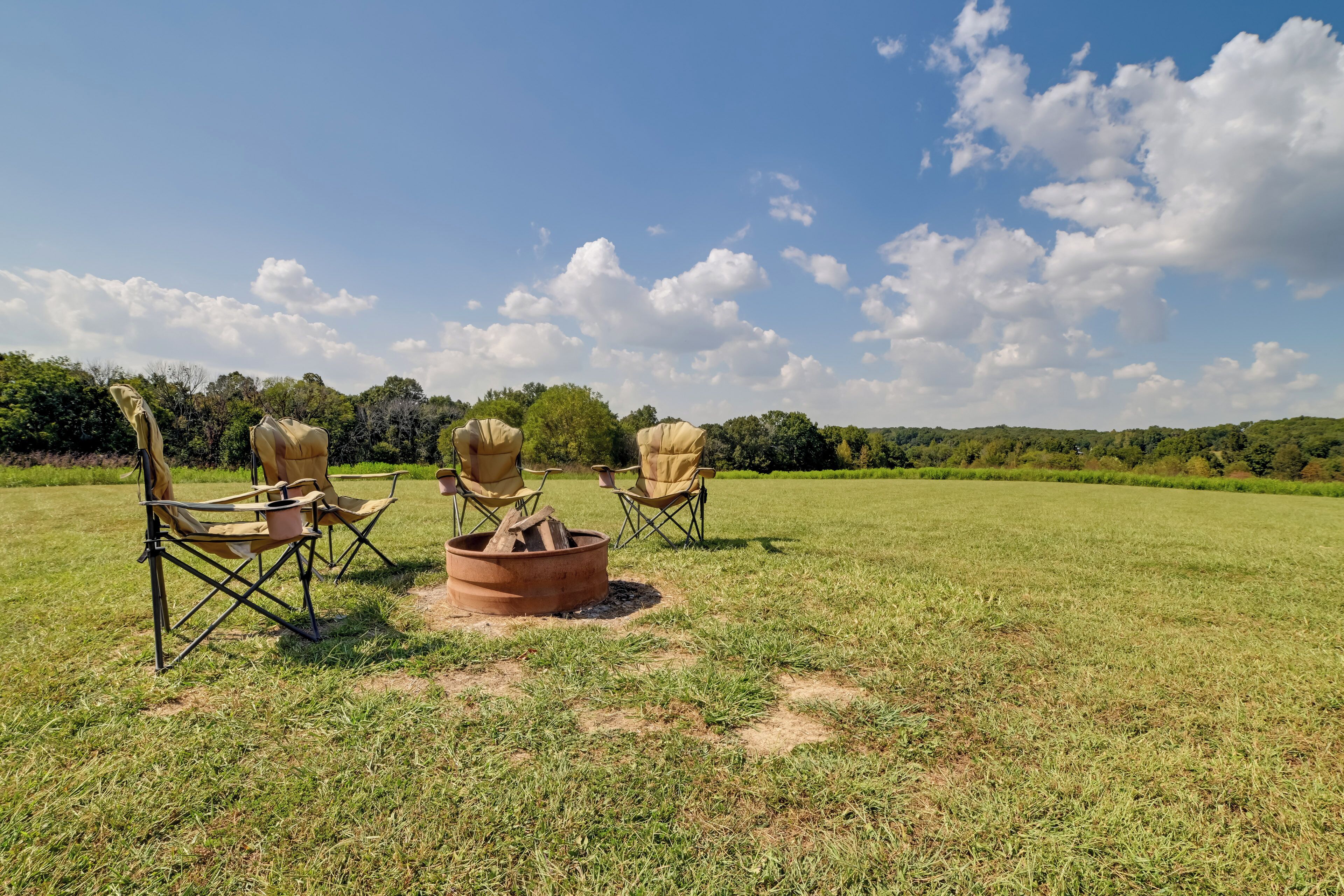 A grassy field with three camping chairs and a fire pit.