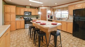 A kitchen with wooden cabinets, a central island with stools, a black refrigerator, and a microwave. - 100-Acre Garden of the Gods Retreat w/ Hot Tub (Elizabethtown)