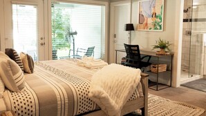Ein Schlafzimmer mit Bett, Schreibtisch, Stuhl, Dusche und einem Fenster mit Jalousien.