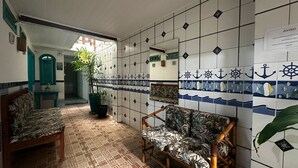 A room with a tiled wall featuring nautical designs, a wooden bench, a potted plant, and a view into another room with a green door.