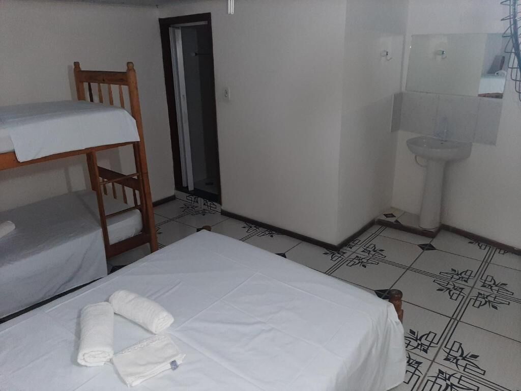 Una habitación pequeña y limpia con una cama individual doble, una cama individual, un baño con lavamanos y un espejo.