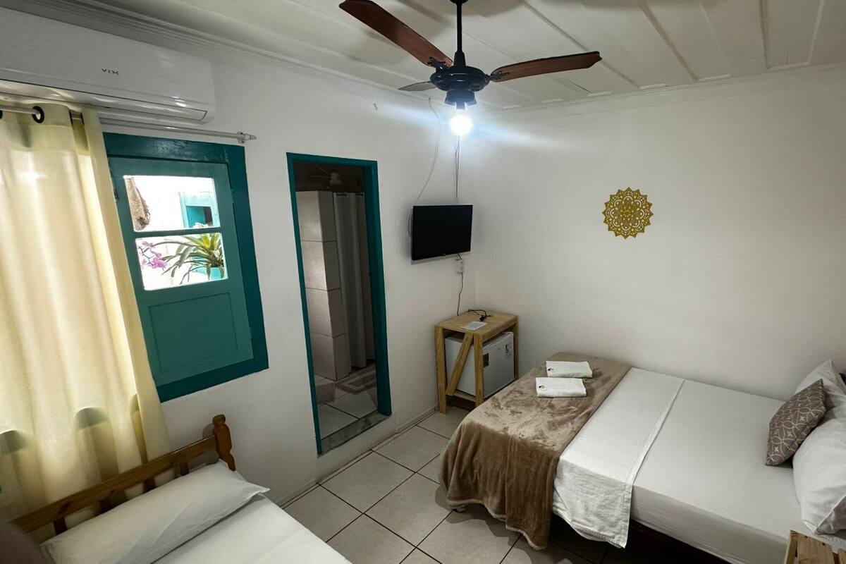 Un dormitorio con cama, ventilador de techo, televisión y una mesita.
