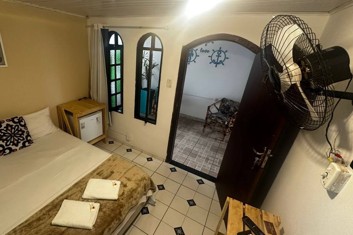 Un dormitorio con una cama, una mesita de noche, un ventilador y vistas al exterior.