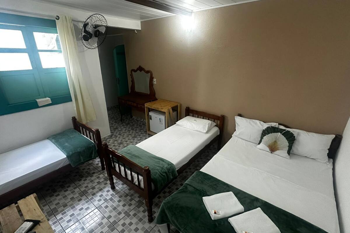 Una habitación con dos camas, una mesita, una silla, un espejo y un ventilador.