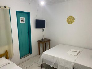 Une pièce comprenant un lit, une petite table, un téléviseur fixé au mur et une porte dotée d’un cadre de couleur turquoise.