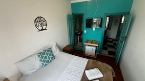 A bedroom with a bed, a small table with a book, a wall-mounted TV, and a refrigerator. - Pousada Real Paraty (Paraty)