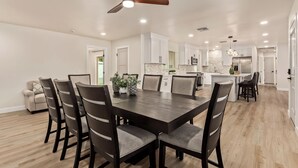 A modern kitchen with white cabinets, a central island, and a dining area with a dark wooden table and chairs. - Modern 4BR Home • Pool • South Scottsdale (Scottsdale)