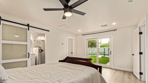 A bedroom with a bed, a ceiling fan, a sliding glass door leading to a balcony, and a glass shower enclosure. - Modern 4BR Home • Pool • South Scottsdale (Scottsdale)